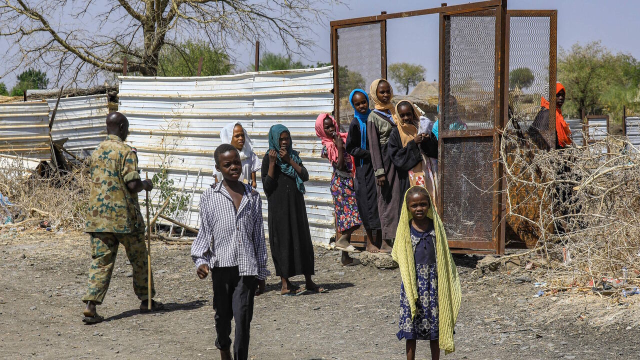 A soldier walks past girls looking on in the village of Dukouli within the Quraysha locality, located in the Fashaqa al-Sughra agricultural region of Sudan's eastern Gedaref state on March 16, 2021. 