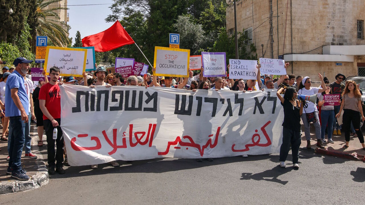 Israeli, Palestinian and foreign activists, hold a banner that reads in Arabic and Hebrew:"Stop the expulsion of families", during a demonstration against Israeli occupation and settlement activity in the Palestinian territories and east Jerusalem, near the Israeli police checkpoint at the entrance of the Shiekh Jarrah neighbourhood, on June 11, 2021.
