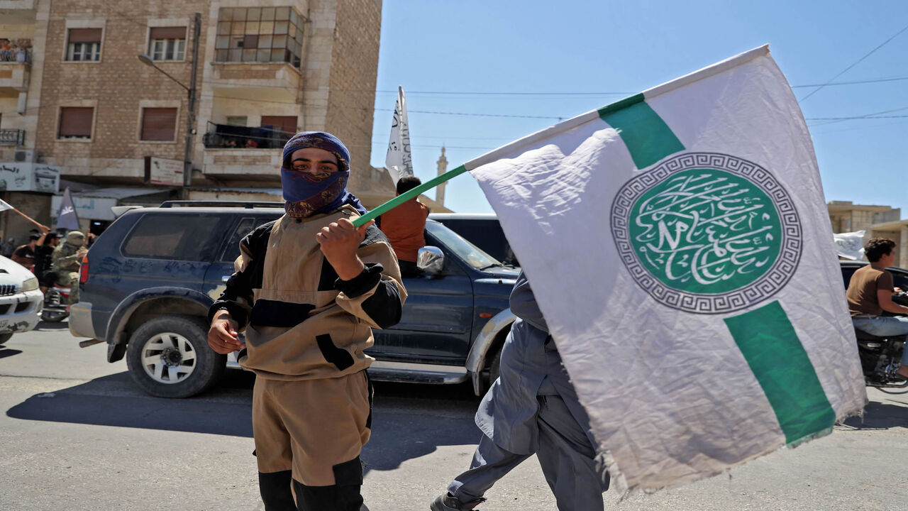 A member of Hayat Tahrir al-Sham holds the group's flag as others parade with their flags and those of the Taliban's declared "Islamic Emirate of Afghanistan" through the rebel-held city of Idlib, Syria, Aug. 20, 2021.