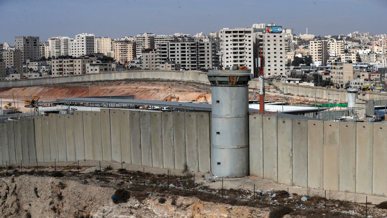 A general view shows a section of Israel's controversial separation wall (bottom) and machinery (L) working on the tarmac of the former Atarot Airport, Nov. 25, 2021.