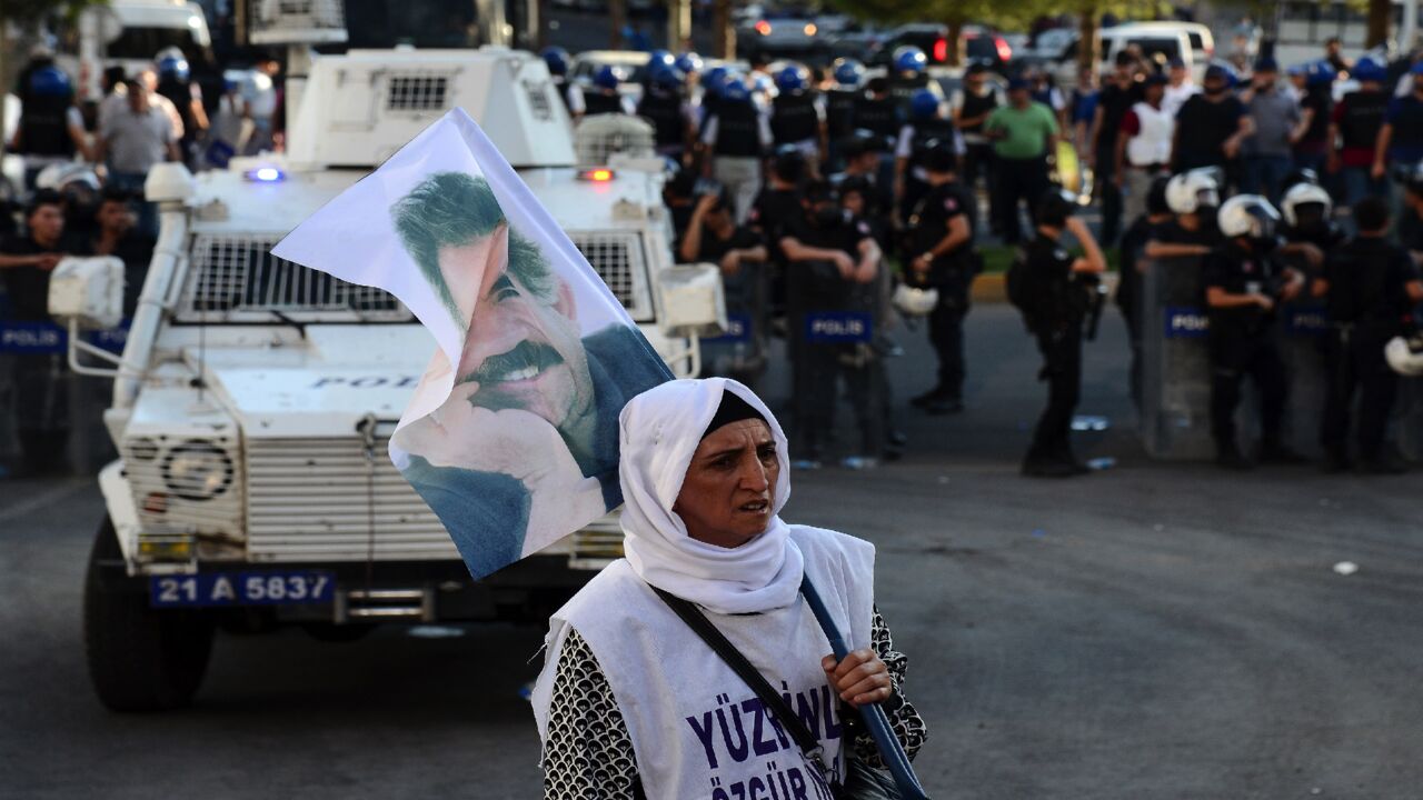 A woman holds a flag of jailed Kurdish leader Abdullah Ocalan as she stands opposite Turkish riot police in Diyarbakir on Aug. 1, 2015.