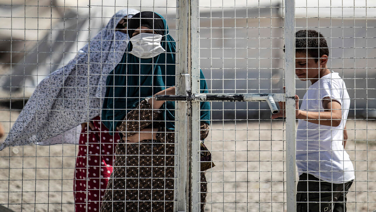 A woman stands by a metal fence at Roj camp that houses family members of people accused to belong to the Islamic State and who were relocated from al-Hol camp, in the countryside near al-Malikiyah, Hasakah province, Syria, Sept. 30, 2020.