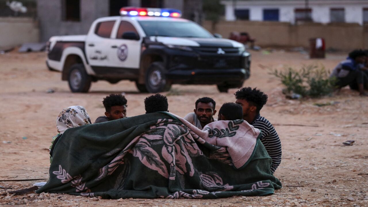 African migrants huddle under a blanket at a makeshift shelter in the capital Tripoli's suburb of Ain Zara, on Oct. 9, 2021.