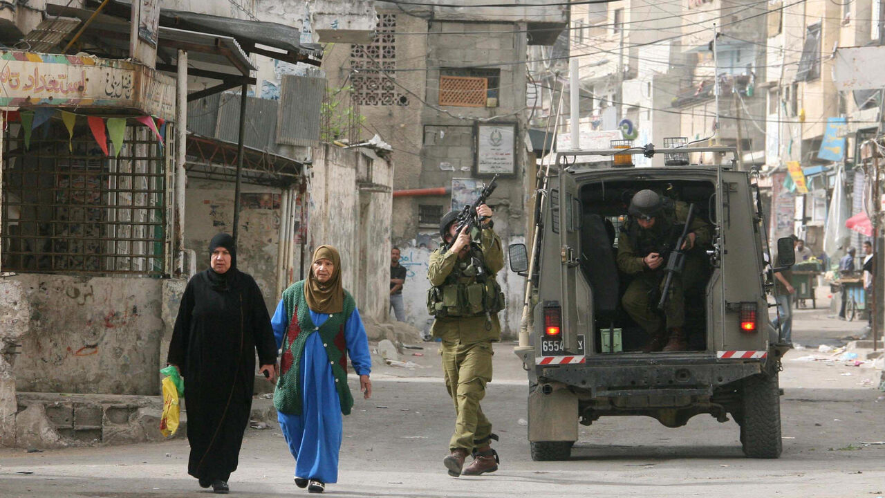 Palestinian women walk past Israeli soldiers taking position during a military operation to arrest militants in the Balata refugee camp near the West Bank city of Nablus, on March 25, 2008.