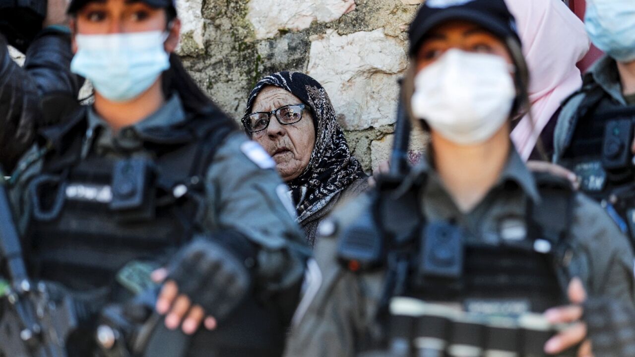 A Palestinian woman stands behind Israeli security forces in the east Jerusalem neighborhood of Sheikh Jarrah on February 13, 2022 A Palestinian woman stands behind Israeli security forces in the east Jerusalem neighborhood of Sheikh Jarrah on February 13, 2022