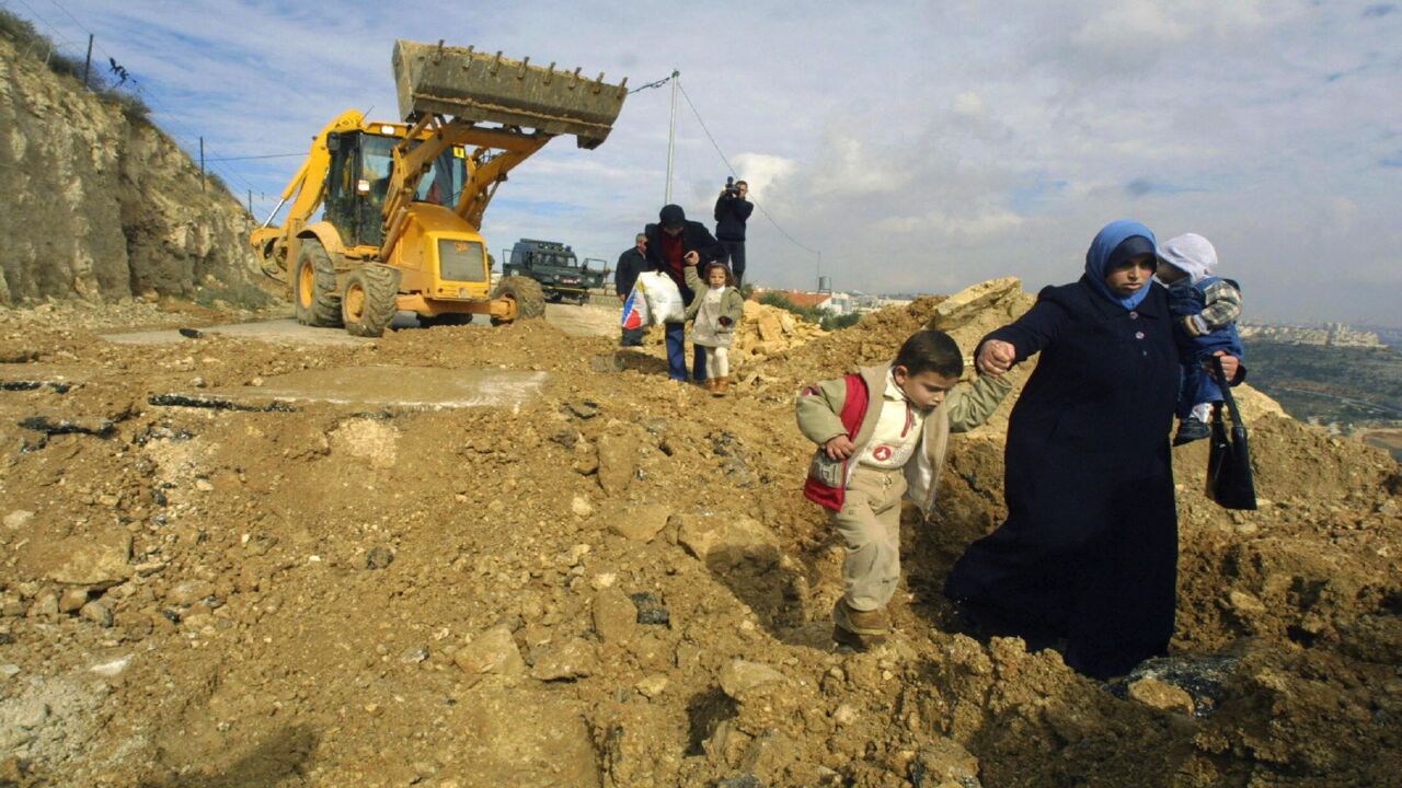 Palestinians walk along a demolished road leading to the Palestinian village of al-Walaja south of Jerusalem, Jan. 11, 2004.