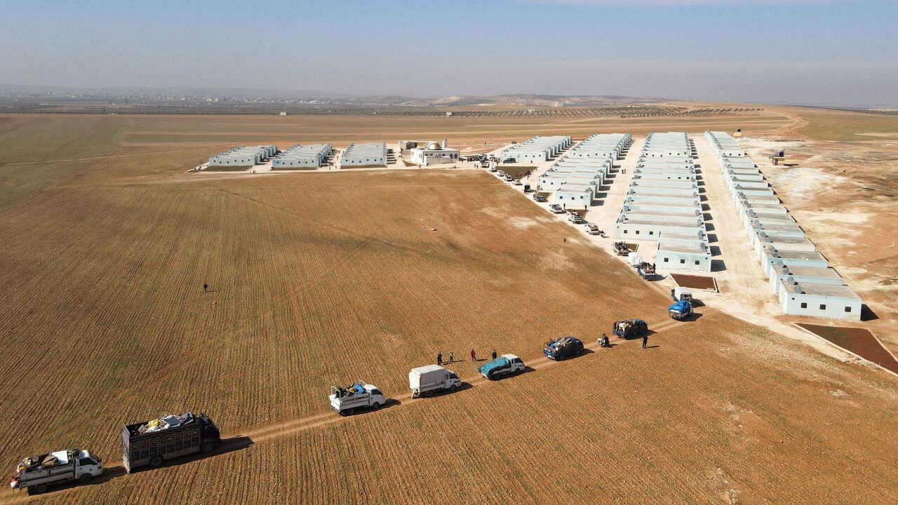 Internally displaced Syrians arriving with their belongings in a convoy of trucks, at a new housing complex. 