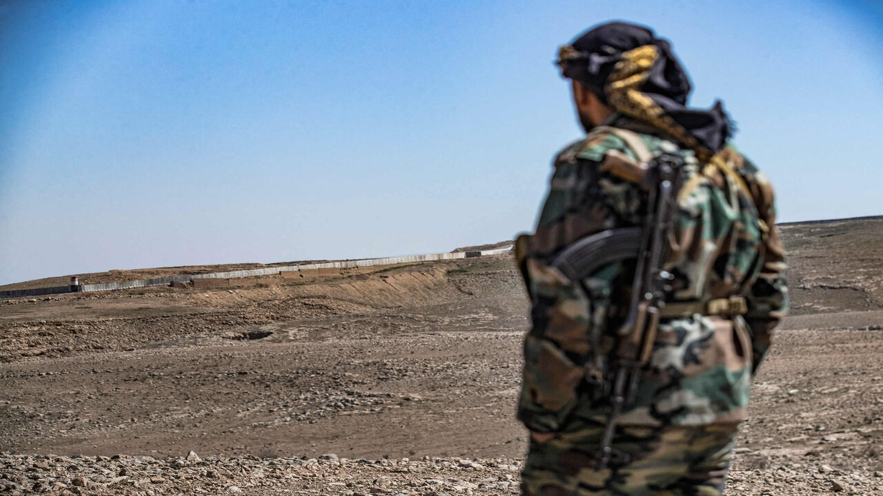 A member of the border guard force loyal to the Syrian Democratic Forces looks from a position in the countryside near the town of al-Hol at construction work on a concrete border fence erected on the Iraqi side, Hasakah province, Syria, March 29, 2022.