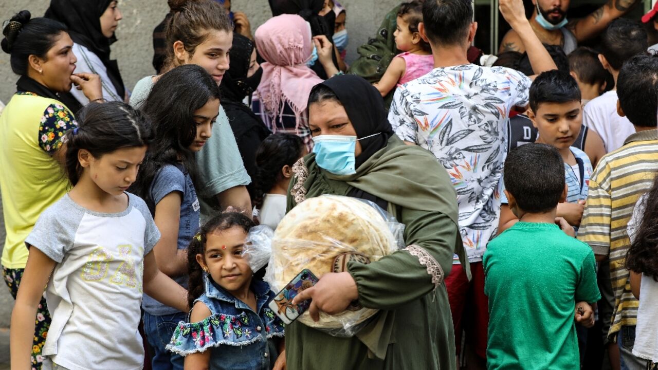 A woman leaves a bakery with a bag of bread as people wait for their turn, in the neighbourhood of Nabaa in the Lebanese capital Beirut's southern suburbs
