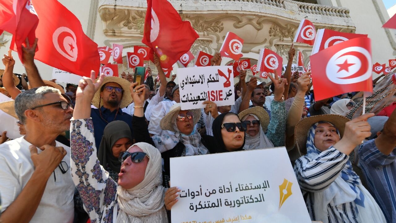 Tunisian protesters raise flags and placards on July 23, 2022, during a demonstration along Habib Bourguiba avenue in the capital Tunis, against their president and the upcoming July 25 constitutional referendum