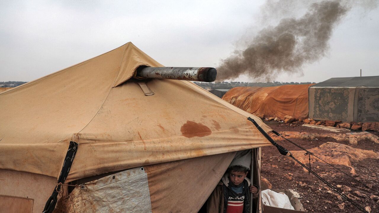 Smoke from an indoor bonfire exits from the chimney of the tent of Umm Raed at a camp for the displaced.