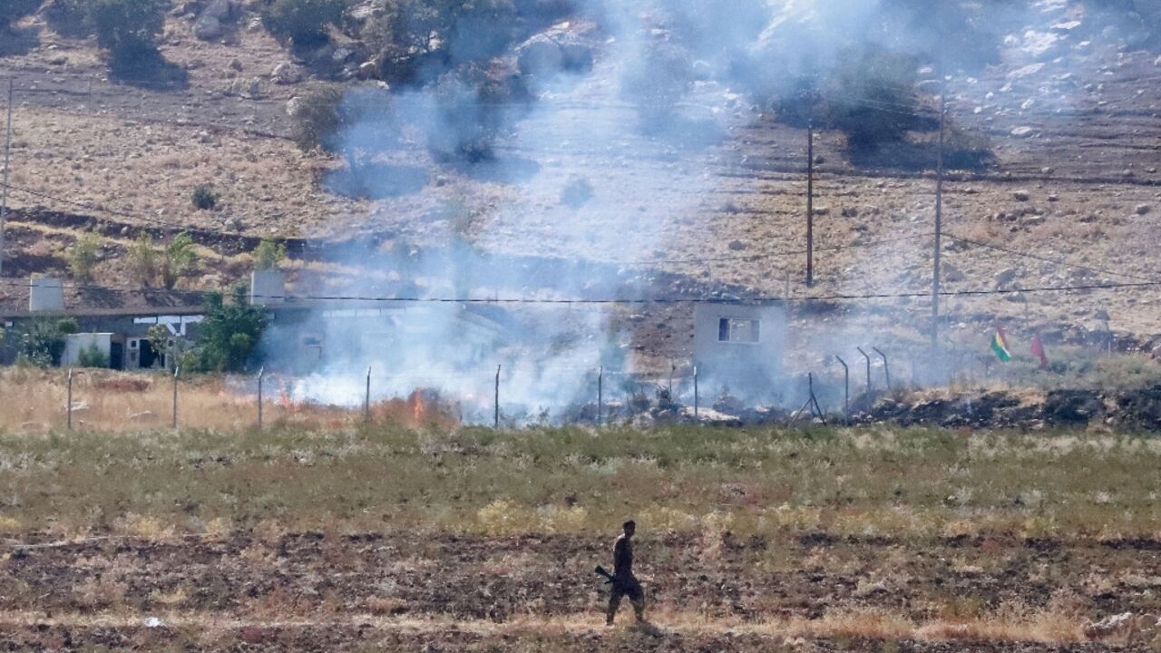 A Kurdish peshmerga fighter walks as smoke billows in the area of Zargwez, outside the Iraqi city of Sulaimaniyah, where several exiled left-wing Iranian Kurdish parties maintain offices