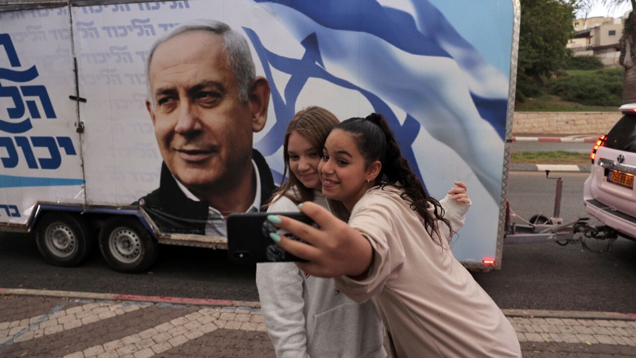Two girls pose for a selfie photo before a vehicle showing Israel's former prime minister Benjamin Netanyahu, ahead of November 1 general elections Two girls pose for a selfie photo before a vehicle showing Israel's former prime minister Benjamin Netanyahu, ahead of November 1 general elections