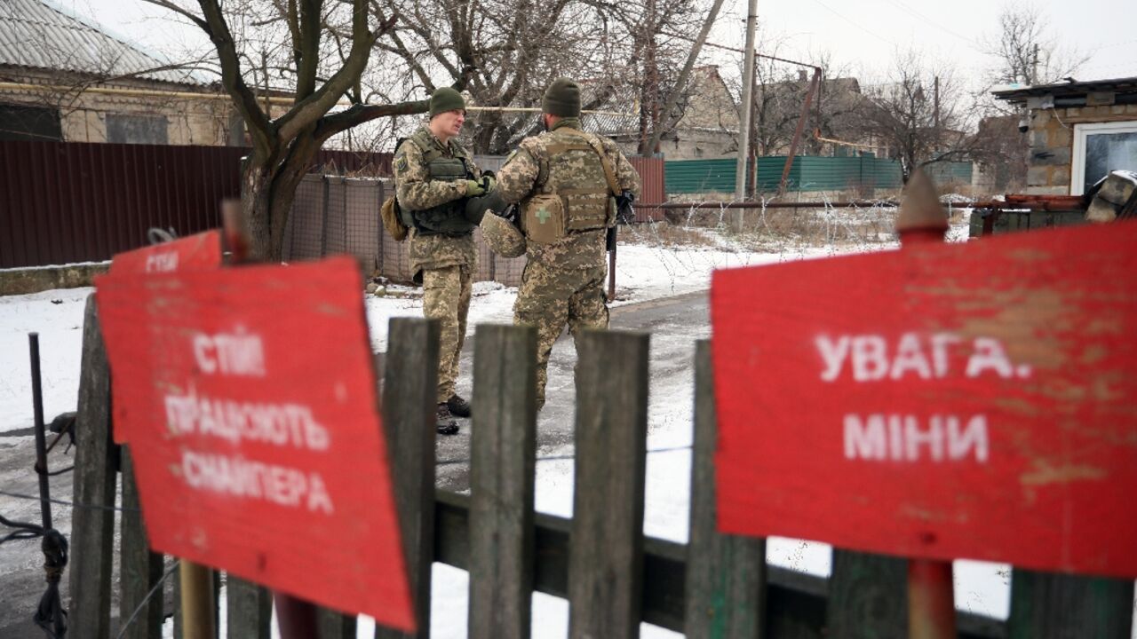 Ukrainian soldiers stand guard near signs reading 'Beware of landmines' 