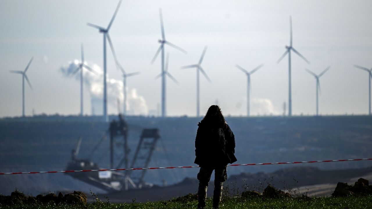 A woman stands on the edge of Germany's Garzweiler lignite open cast mine on November 12, 2022, with wind turbines in the background