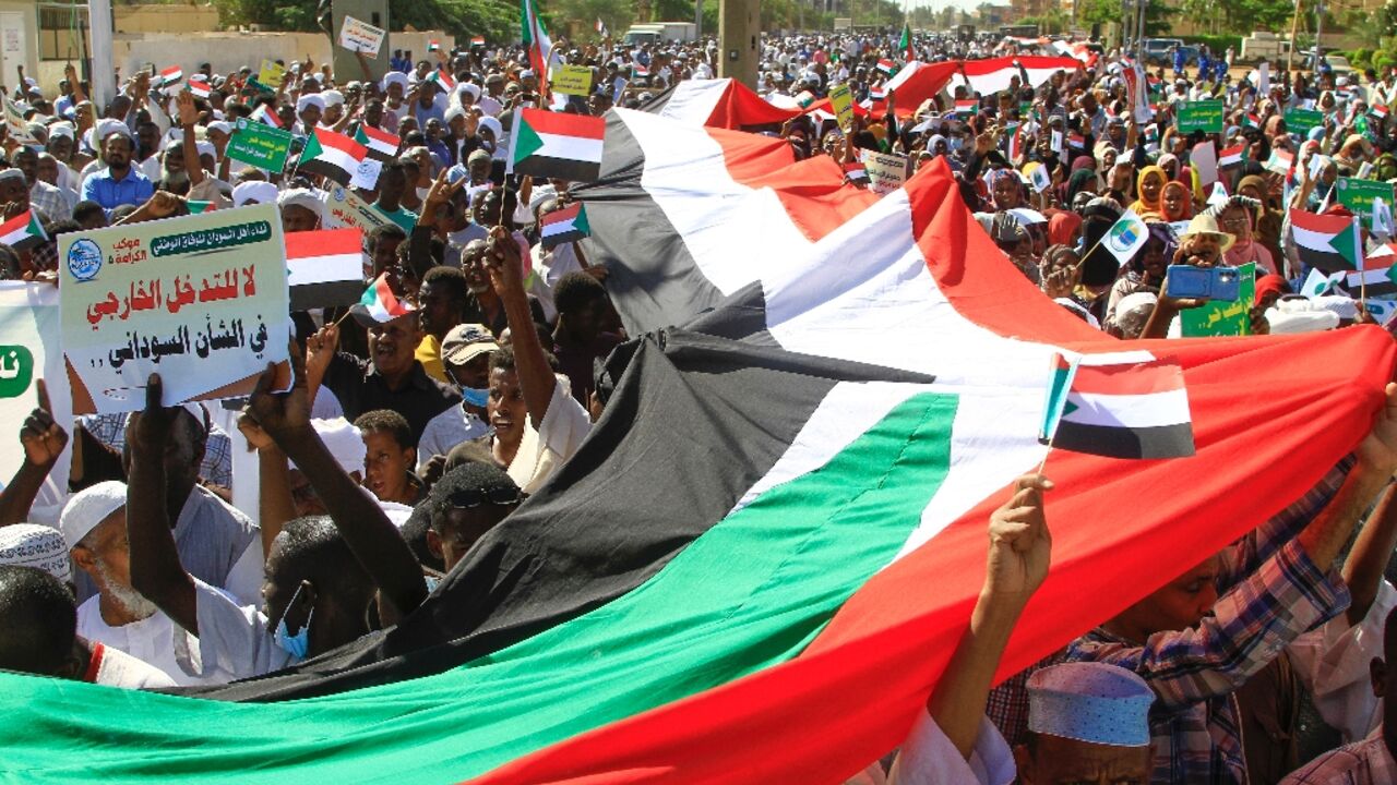 Sudanese protesters deploy a giant national flag, as they march outside the UN headquarters in Khartoum on December 3