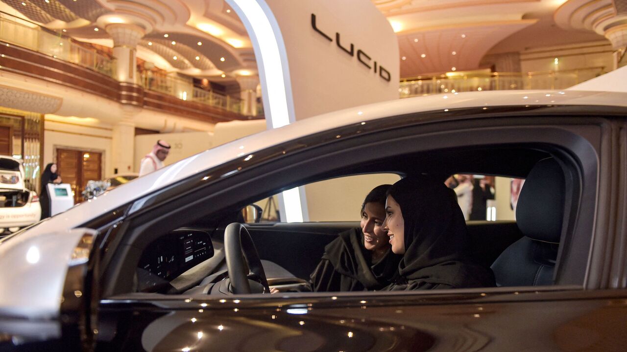 A picture taken on July 14, 2022, ahead of a visit by the United States' president to Saudi Arabia, shows hostesses in a car manufactured by US electric vehicle maker Lucid Group at the KSA Green Transition Journey exhibition in the Red Sea port of Jeddah. - A exhibiton offered a presentation on the Saudi Green Initiative, which also includes goals for tree-planting and reducing emissions. (Photo by Amer HILABI / AFP) (Photo by AMER HILABI/AFP via Getty Images)