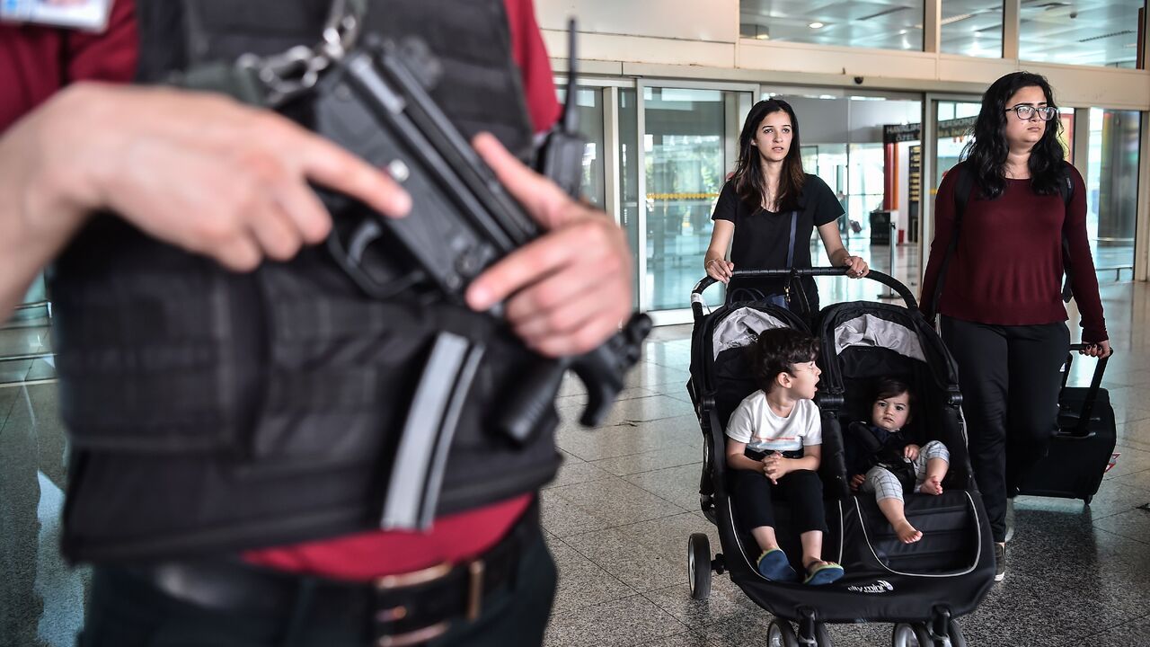 An armed Turkish security officer (L) stands guard near a gate as passengers walk past within a memorial ceremony on June 28, 2017 at Ataturk International airport in Istanbul, one year since the triple suicide bombing and gun attack by Islamic State (IS) jihadists.  (OZAN KOSE/AFP via Getty Images)