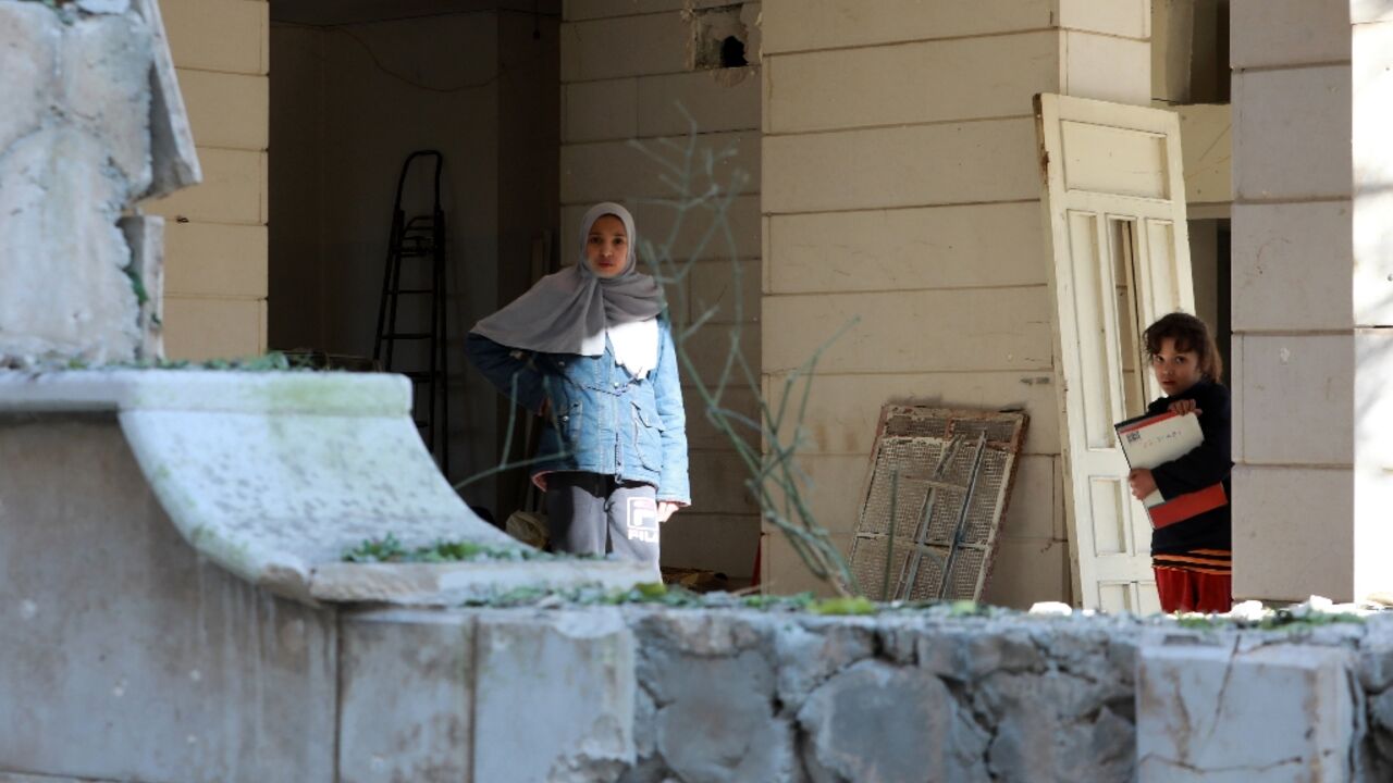 Two young girls stand in front of a building hit by a reported Israeli missile strike in Damascus, on February 19, 2023