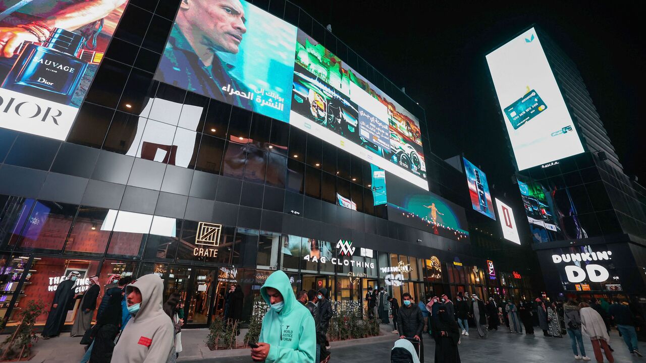 People walk beneath advertisement billboards at Boulevard entertainment city in the Saudi capital Riyadh, late on January 19, 2022. (Photo by FAYEZ NURELDINE/AFP via Getty Images)