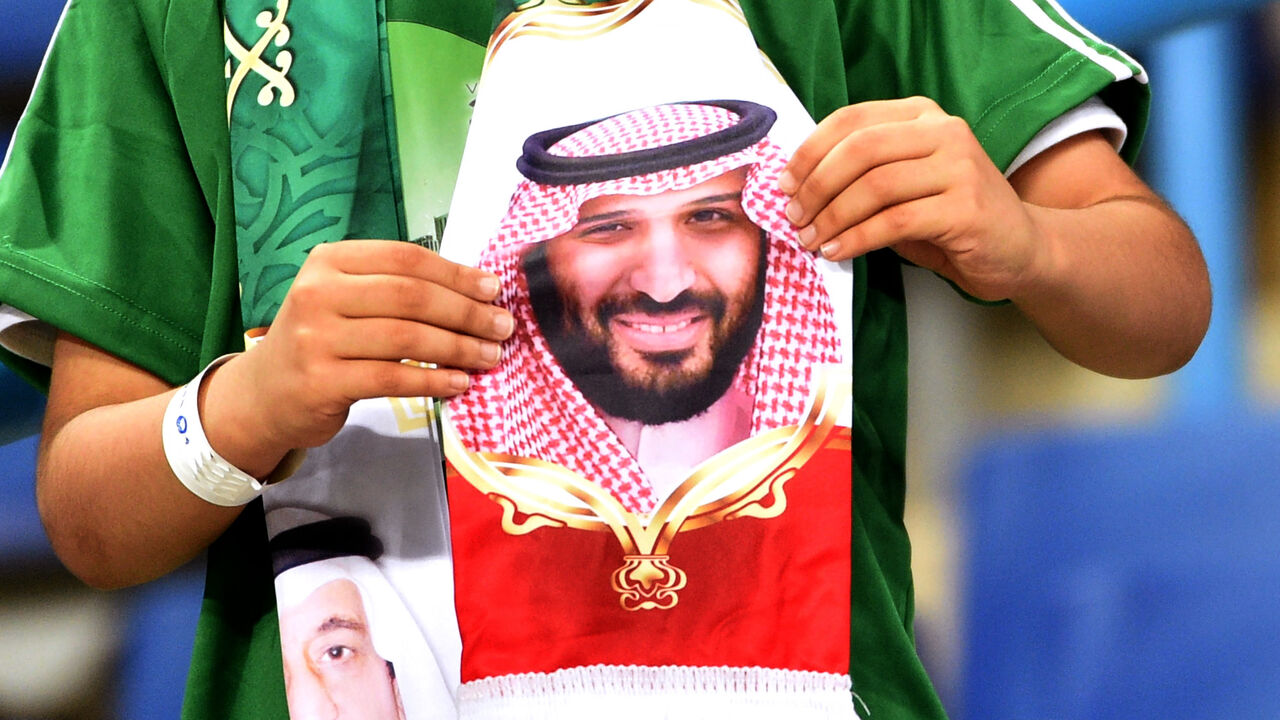 A Saudi fan holds a scarf with portraits of King Salman (L) and his son, Crown Prince Mohammed bin Salman.