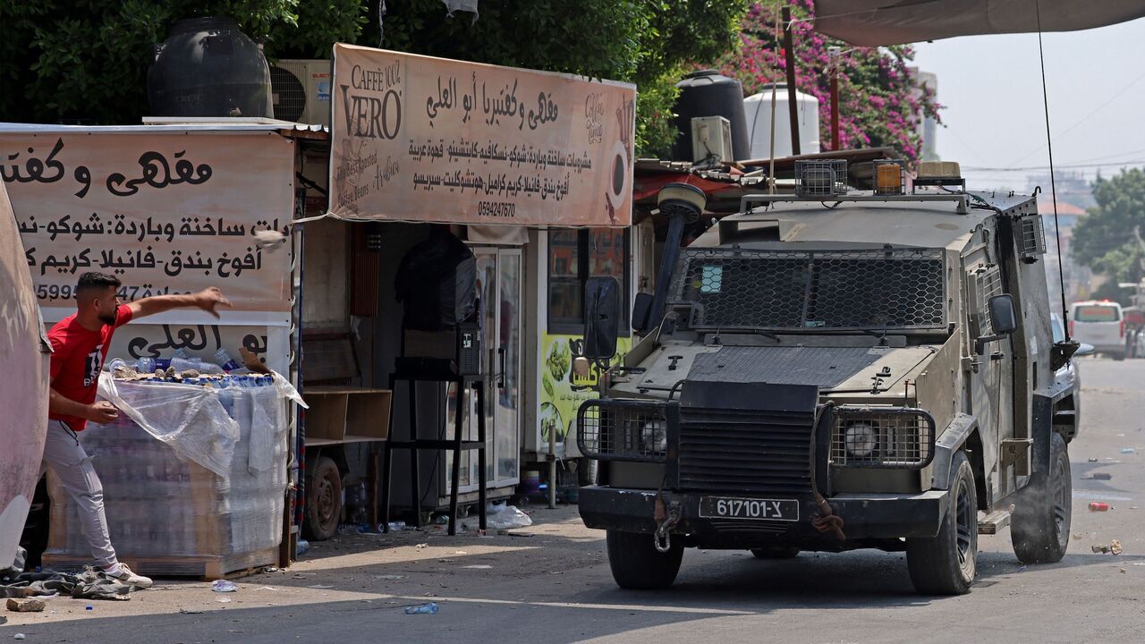A Palestinian man throws a stone at an armored vehicle during an Israeli military operation in the occupied West Bank city of Jenin, on July 3, 2023.