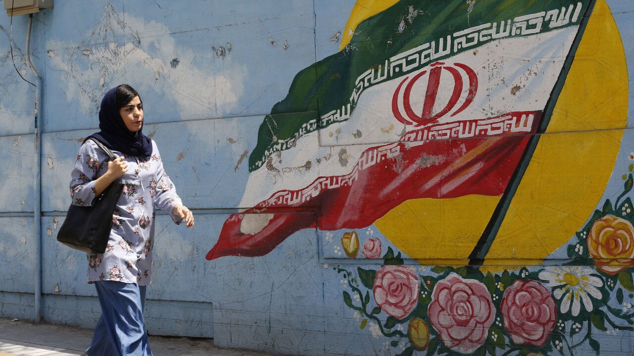 A woman walks in front of a mural painting depicting the Iranian flag, in the capital Tehran on August 6, 2018.