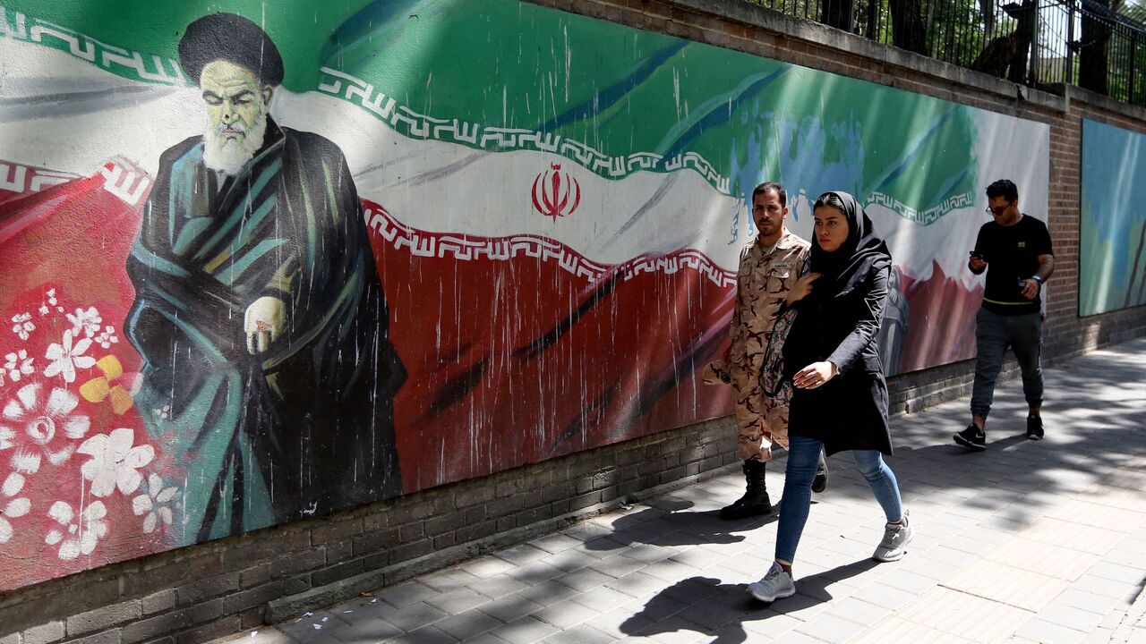 People walk past a mural painting showing the founder of the Islamic republic Ayatollah Ruhollah Khomeini and the national flag along the wall of the former US embassy in the Iranian capital Tehran on June 22, 2019. 