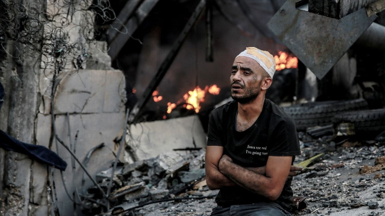 An injured man sits in front of a smouldering building in the aftermath of an Israeli strike on Gaza City on Thursday