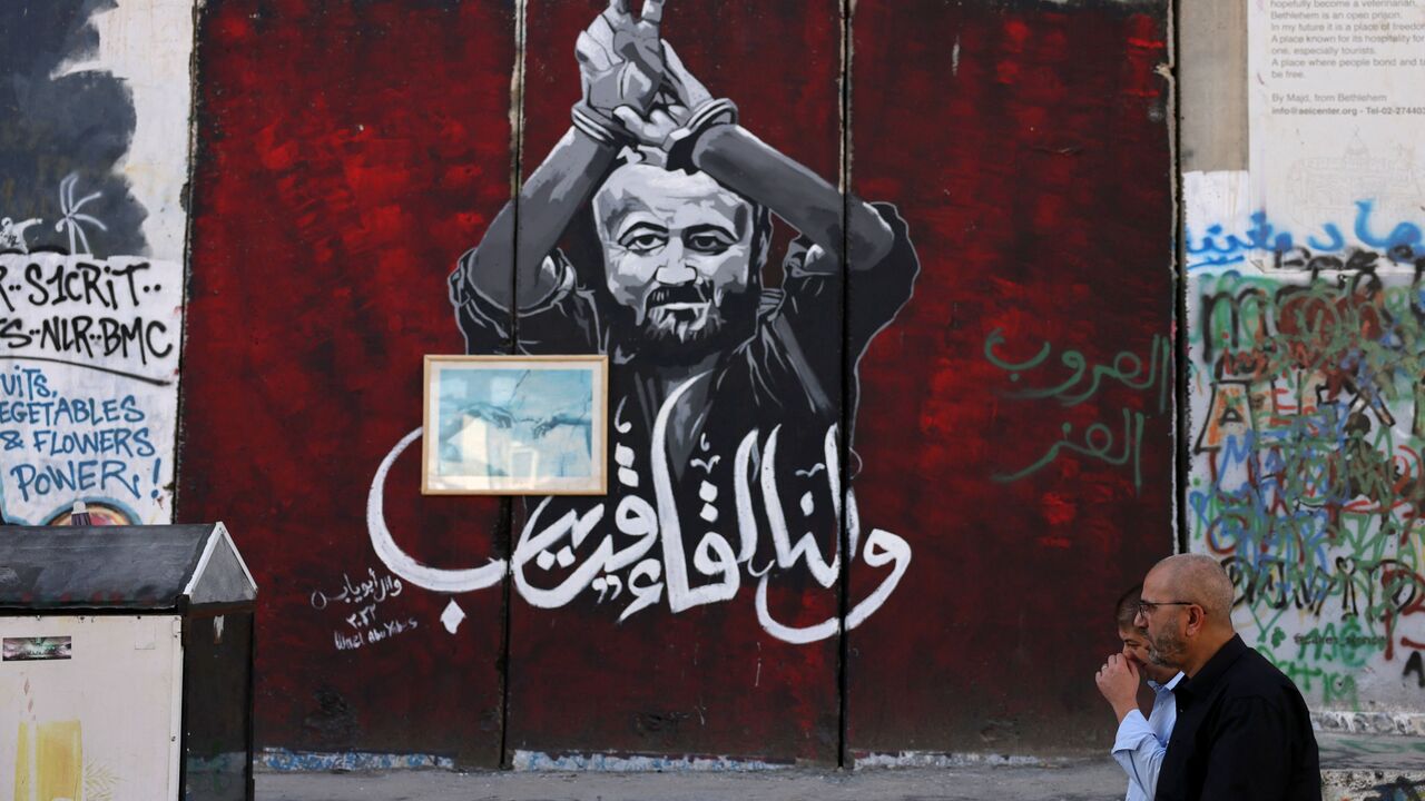 Men walk past a section of Israel's separation barrier painted with a portrait of Palestinian Marwan Barghouti, held in an Israel jail, on November 6, 2023 in Bethlehem in the occupied West Bank.