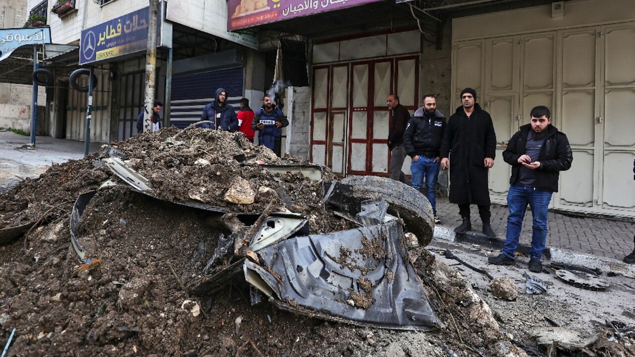 Palestinian onlookers survey the mangled wreckage of a car hit by an Israeli air strike targeting a top militant near the Balata refugee camp in the West Bank city of Nablus