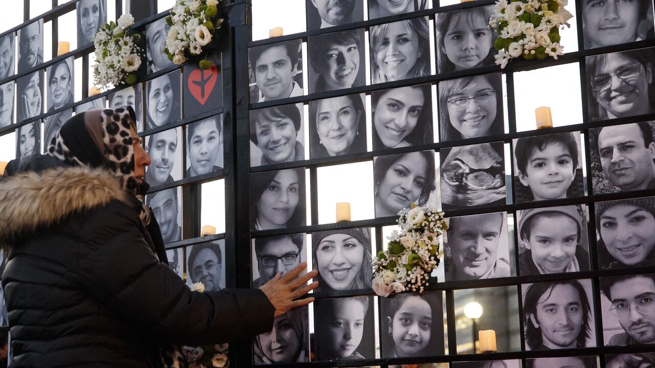 A woman touches victims' portraits as mourners attend an outdoor vigil for the victims of Ukrainian passenger jet flight PS752.