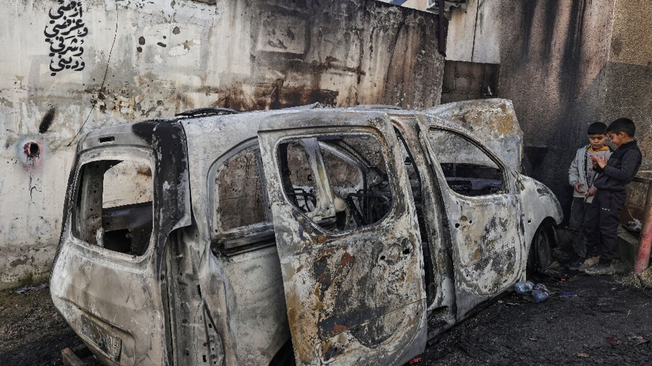 Palestinian children stand next to a burnt out vehicle following an Israeli raid on the West Bank city of Jenin and its adjacent refugee camp