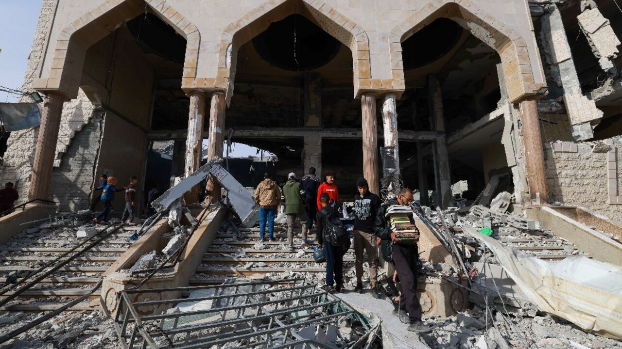 A man walks with salvaged religious books among the rubble of a mosque following Israeli bombardment in Rafah