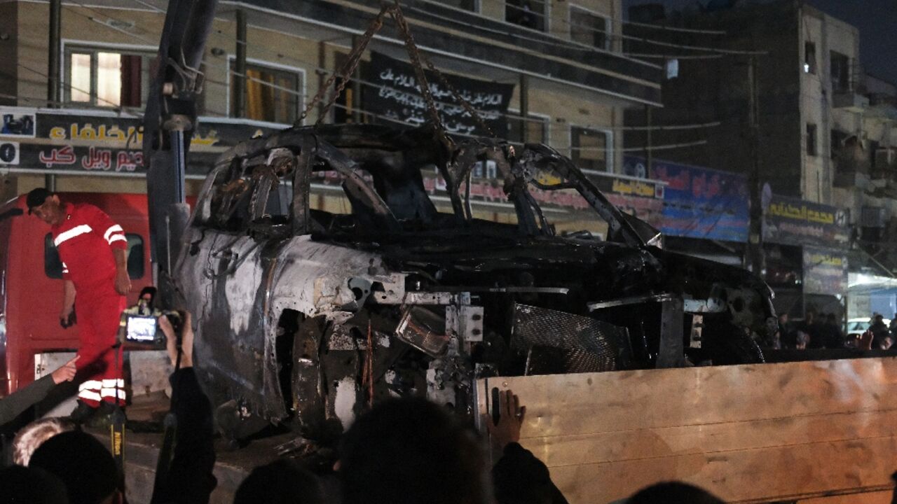 People watch as a vehicle that was hit by a drone strike killing three people including two leaders of a pro-Iran group is removed from a Baghdad neighbourhood