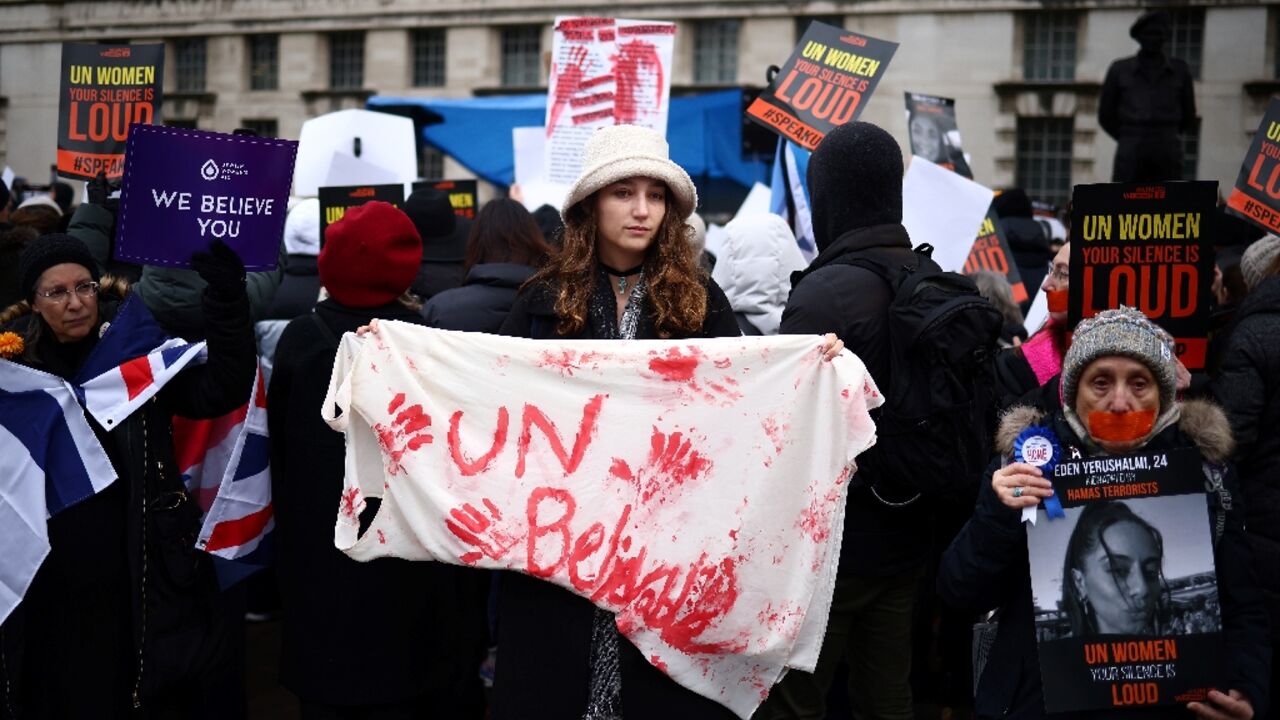 Demonstrators hold posters reading "UN Women, your silence is loud" along with a red paint-stained sheet reading "UNbelievable" 