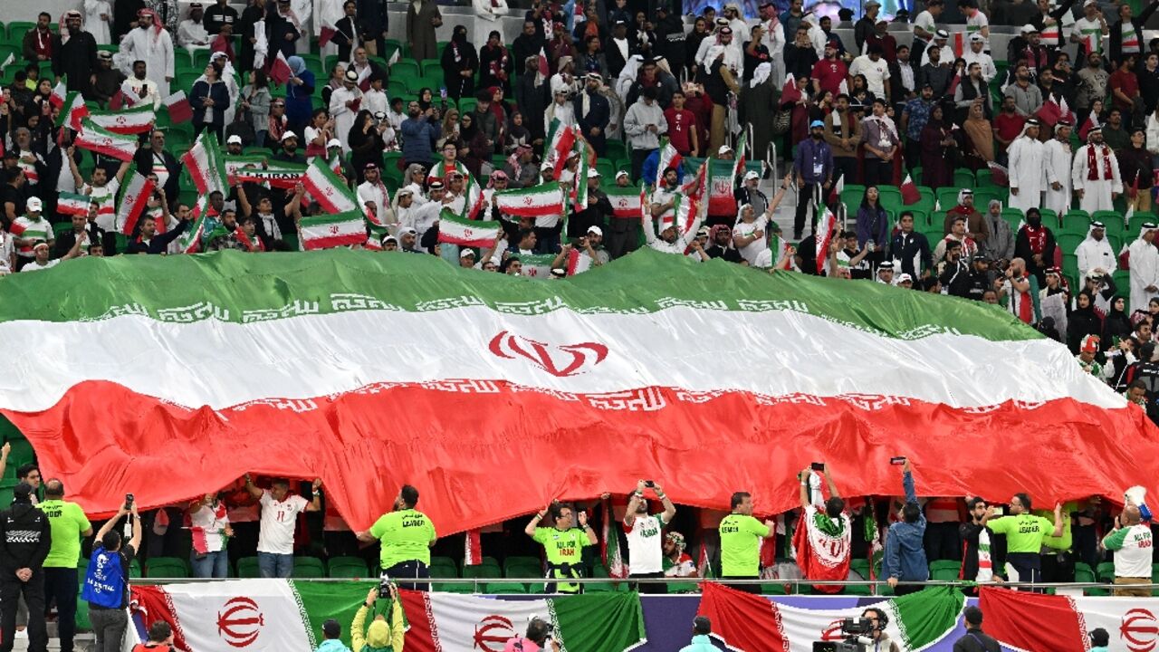 Iranian football fans hold up the national flag during Asian Cup semi-final against Qatar in Doha in  February