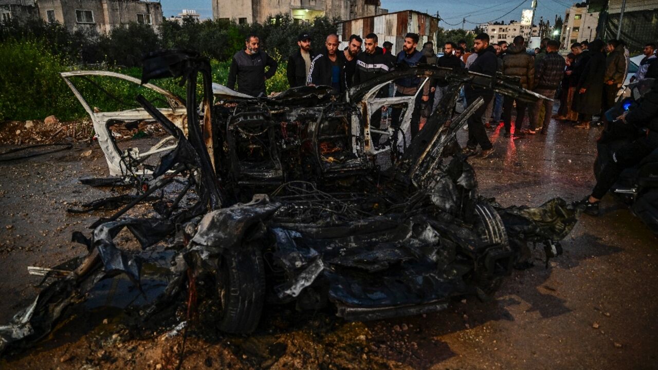 Palestinian men surround a charred car hit in an Israeli air strike on Jenin