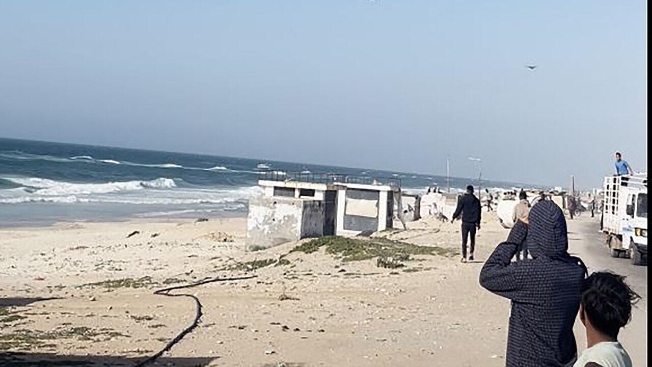 In this image grab from an AFPTV video, people watch as a US aircraft carrying food parcels flies above a beach in the Gaza Strip before dropping the humanitarian aid attached to parachutes, on March 2, 2024. Israel's top ally the United States said it began air-dropping aid into war-ravaged Gaza on March 2, as the Hamas-ruled territory's health ministry reported more than a dozen child malnutrition deaths. (Photo by AFP) (Photo by -/AFP via Getty Images)