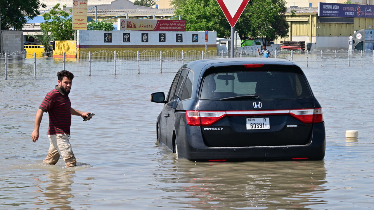 A man walks past a stranded car on a flooded street in Dubai following heavy rains on April 18, 2024.