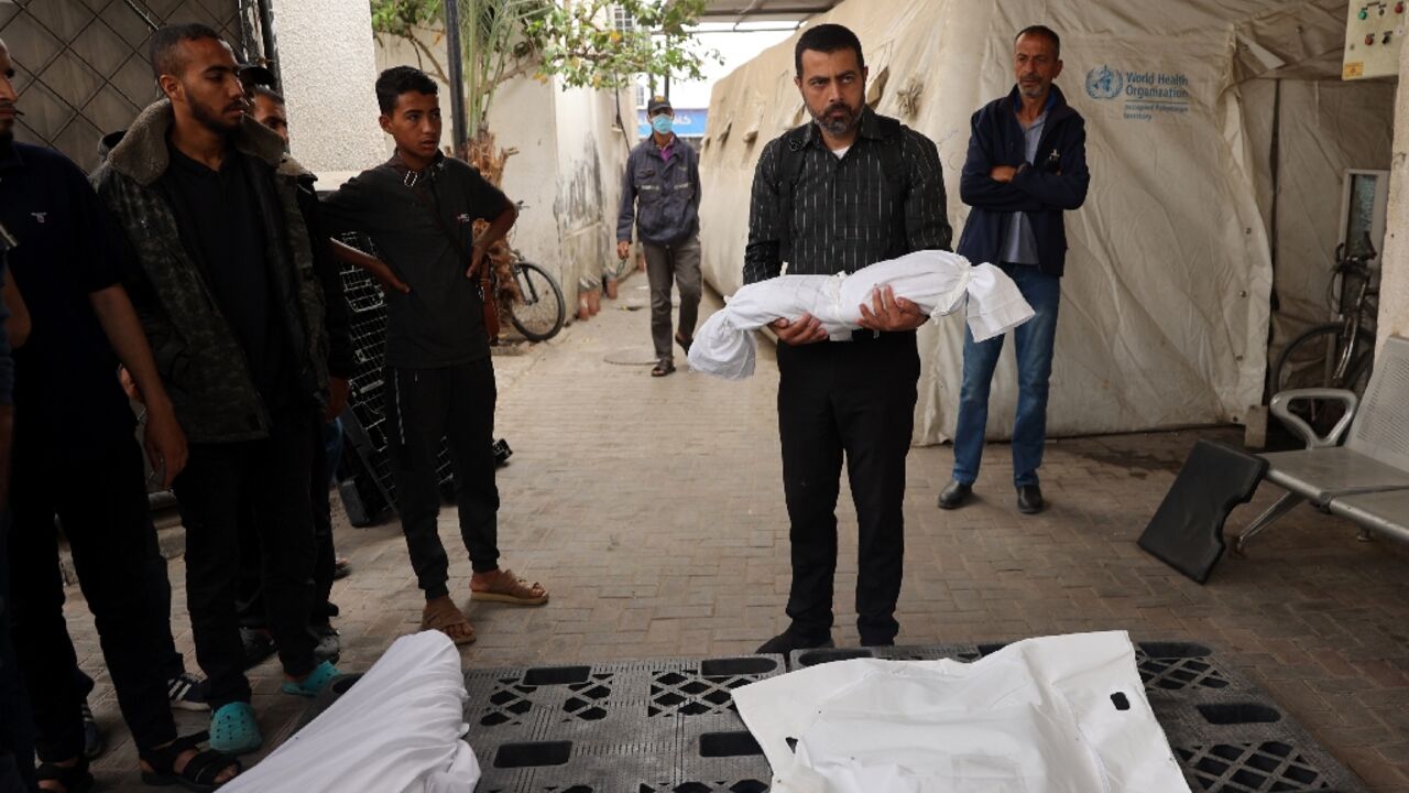 Outside the morgue of a hospital in Rafah, the southern Gaza Strip, a man carries the shrouded body of a child killed in Israeli bombardment