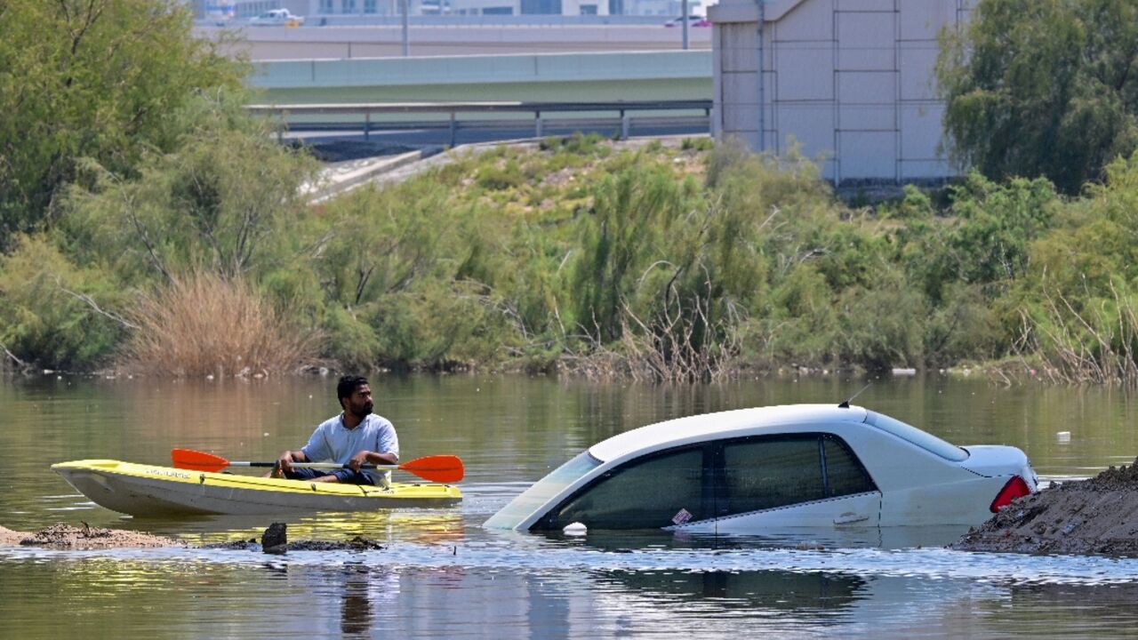 A man steers his canoe past a stranded car on a flooded street in Dubai