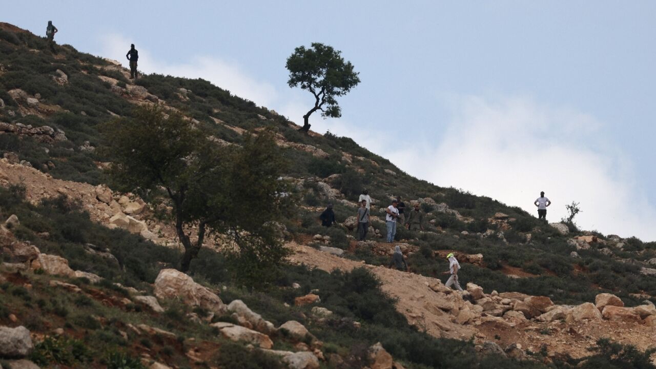 Armed Israeli settlers gather on a hill overlooking Al-Mughayyir village