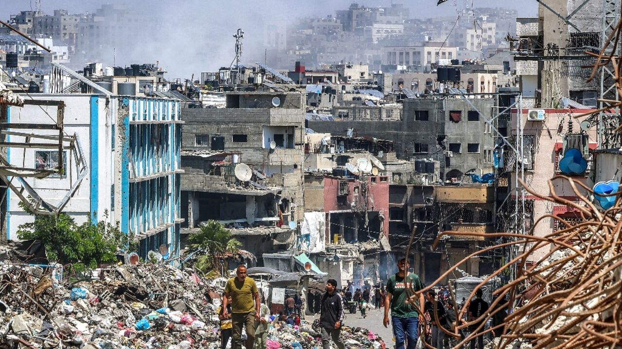 People walk past a mound of trash and destroyed buildings as smoke rises during Israeli bombardment in Jabalia, northern Gaza