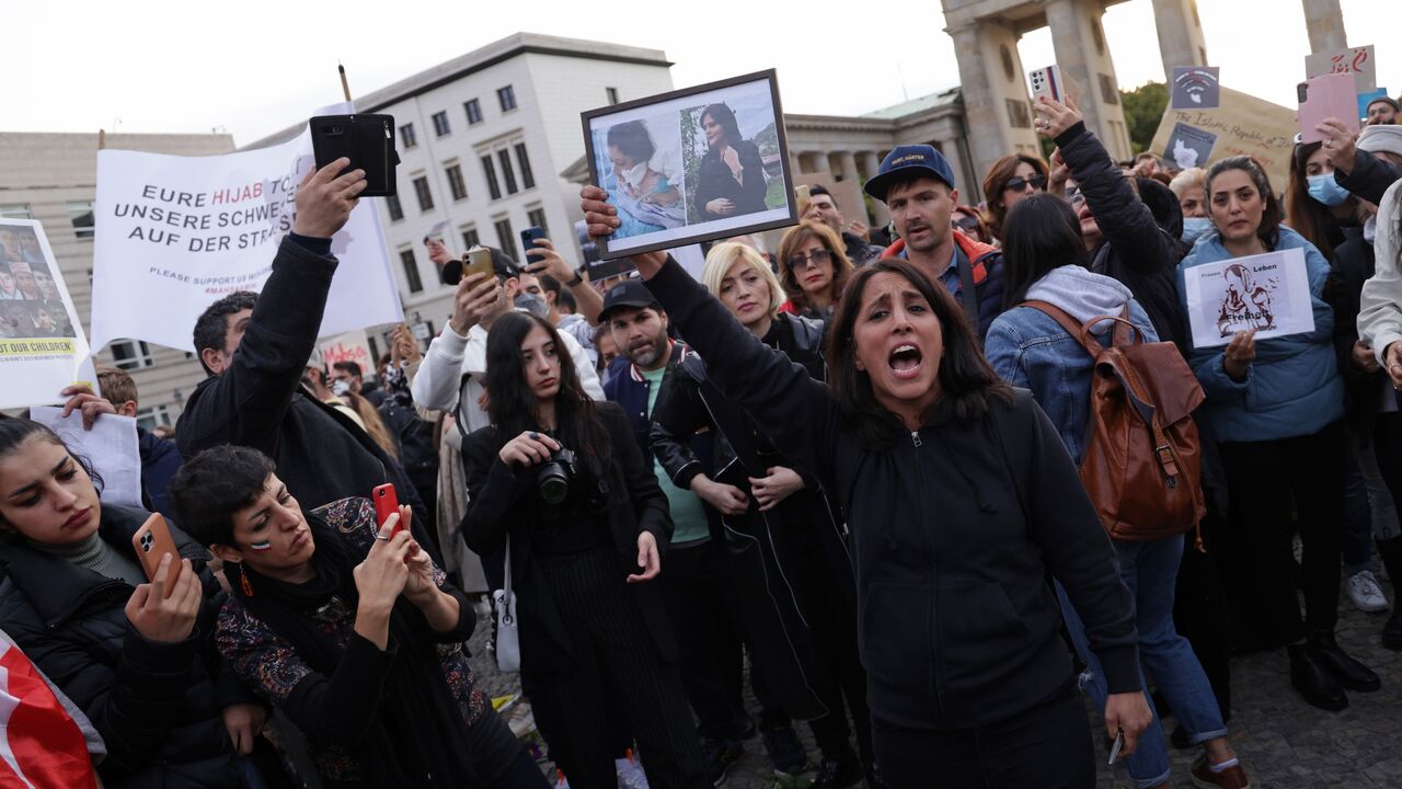 A female protester holds up photographs of Mahsa Amini before cutting her hair with scissors as an act of solidarity with women in Iran during a demonstration against the death Amini on Sep. 23, 2022, in Berlin, Germany.