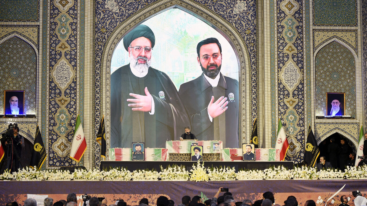 An Iranian man reads a prayer over the coffins of late president Ebrahim Raisi (portrait top L) and late governor of Iran's East Azerbaijan Province Malik Rahmati (portrait top R) during a funeral ceremony at the Imam Reza shrine, in the city of Mashhad, on May 23, 2024.