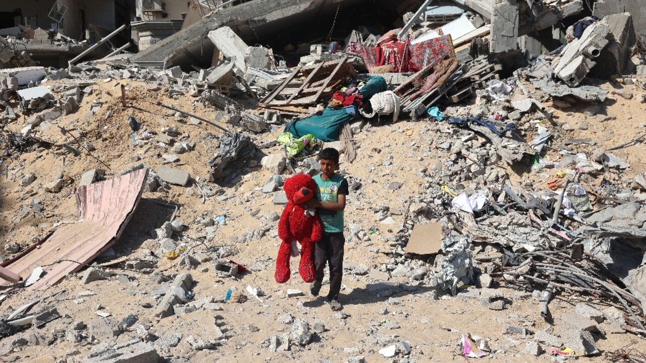 A Palestinian child walks with a toy bear recovered from the rubble of a destroyed building following Israeli bombardment in Khan Yunis, southern Gaza