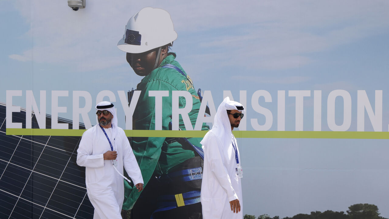 Men wearing thawbs walk past a billboard promoting the transition to renewable energies at the UNFCCC COP28 Climate Conference the day before its official opening on November 29, 2023 in Dubai, United Arab Emirates. The COP28 is bringing together stakeholders, including international heads of state and other leaders, scientists, environmentalists, indigenous peoples representatives, activists and others to discuss and agree on the implementation of global measures towards mitigating the effects of climate c