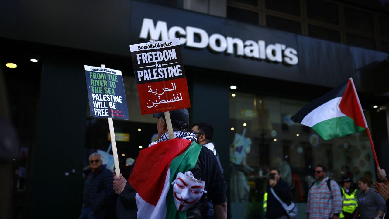 Pro-Palestinian activists and supporters wave flags and hold placards along with a Guy Fawkes mask as they walk past a McDonald's during a protest in central London on March 30, 2024, calling for a cease-fire in the Israel-Hamas conflict. 