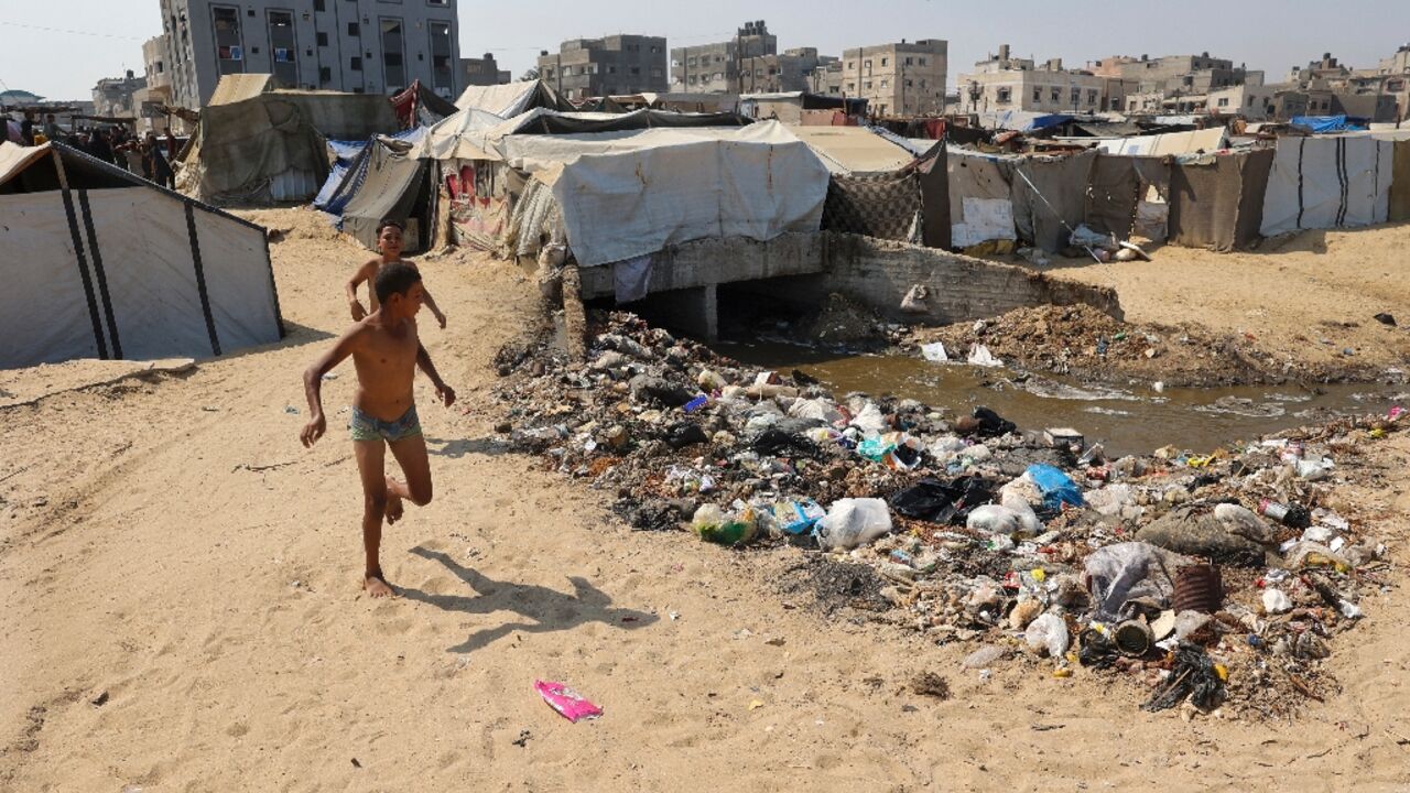 Children play next to garbage and sewage at a camp for displaced Palestinians in Deir el-Balah, central Gaza